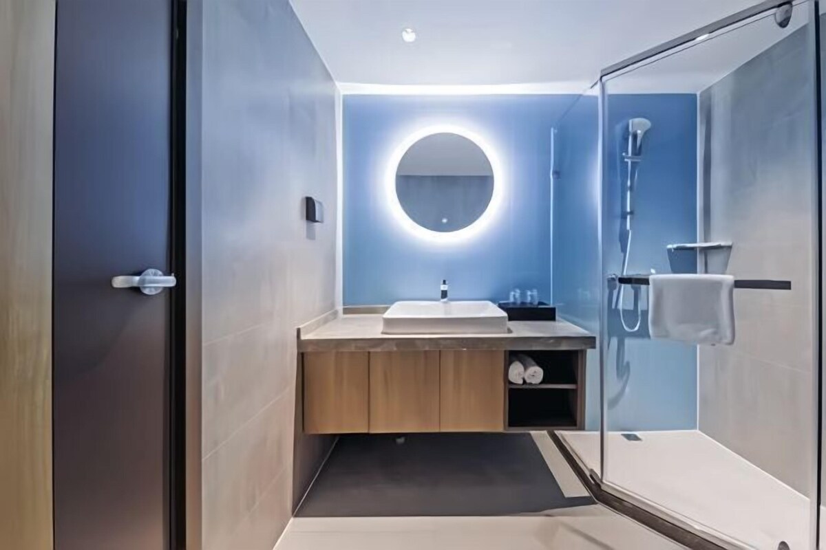 A modern bathroom with a glass shower enclosure, a round mirror, and a wooden vanity.