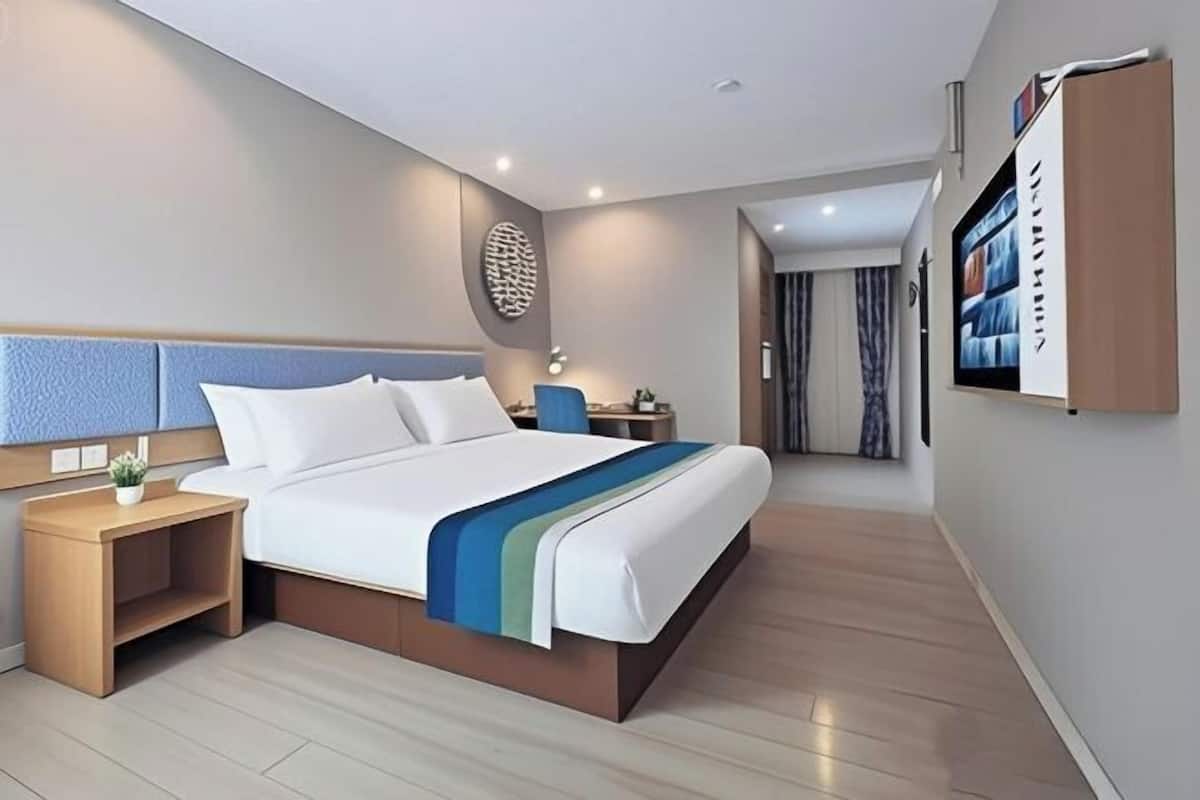 A modern hotel room with a bed, bedside tables, a TV, and a wall-mounted shelf.