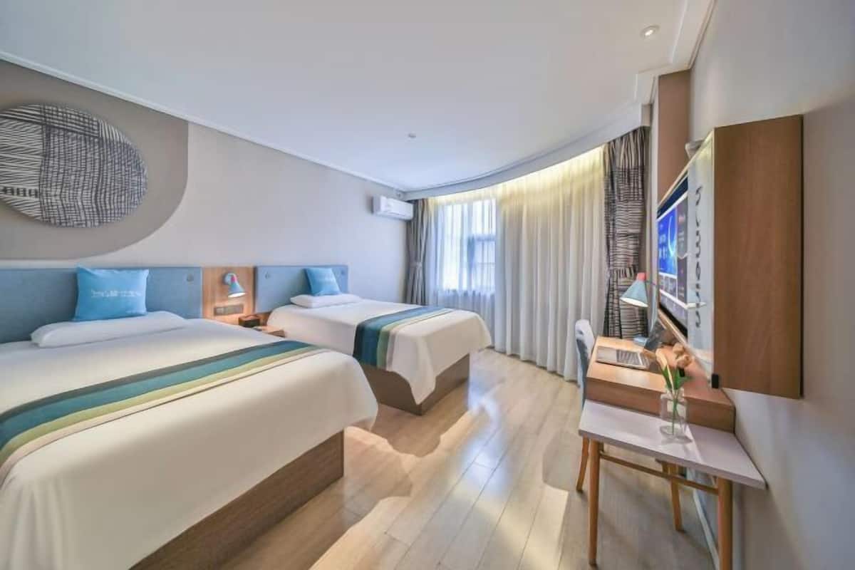 A hotel room with two beds, a desk, a wall-mounted TV, and a large abstract artwork.