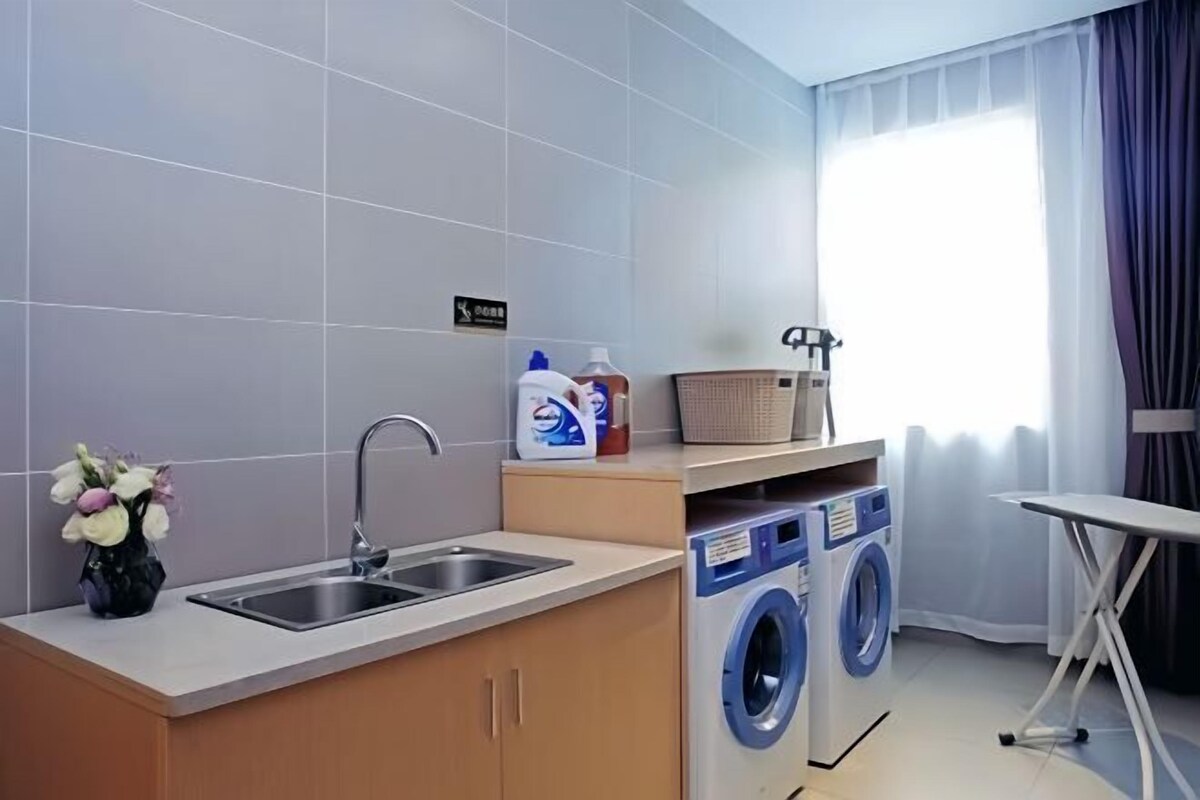A compact hotel room with a kitchenette, a washing machine, and a small ironing station.