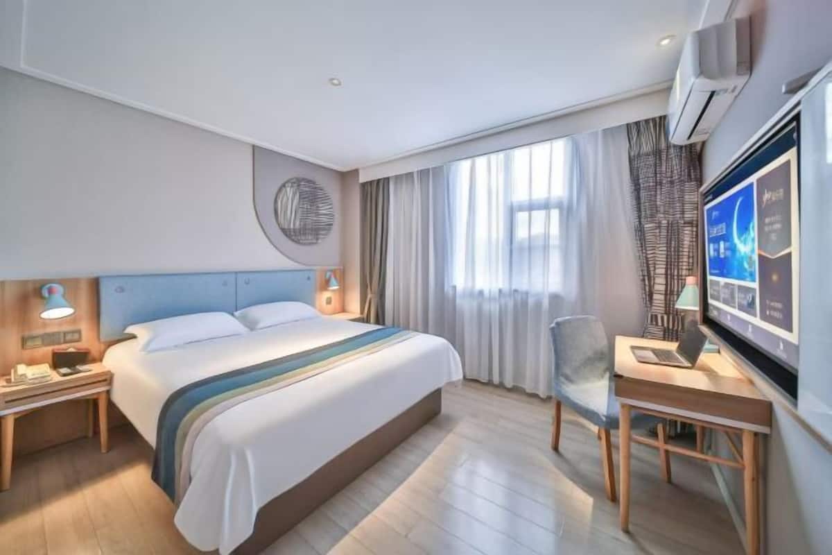 A hotel room with a bed, a desk, a chair, a TV, and a wall-mounted air conditioner.