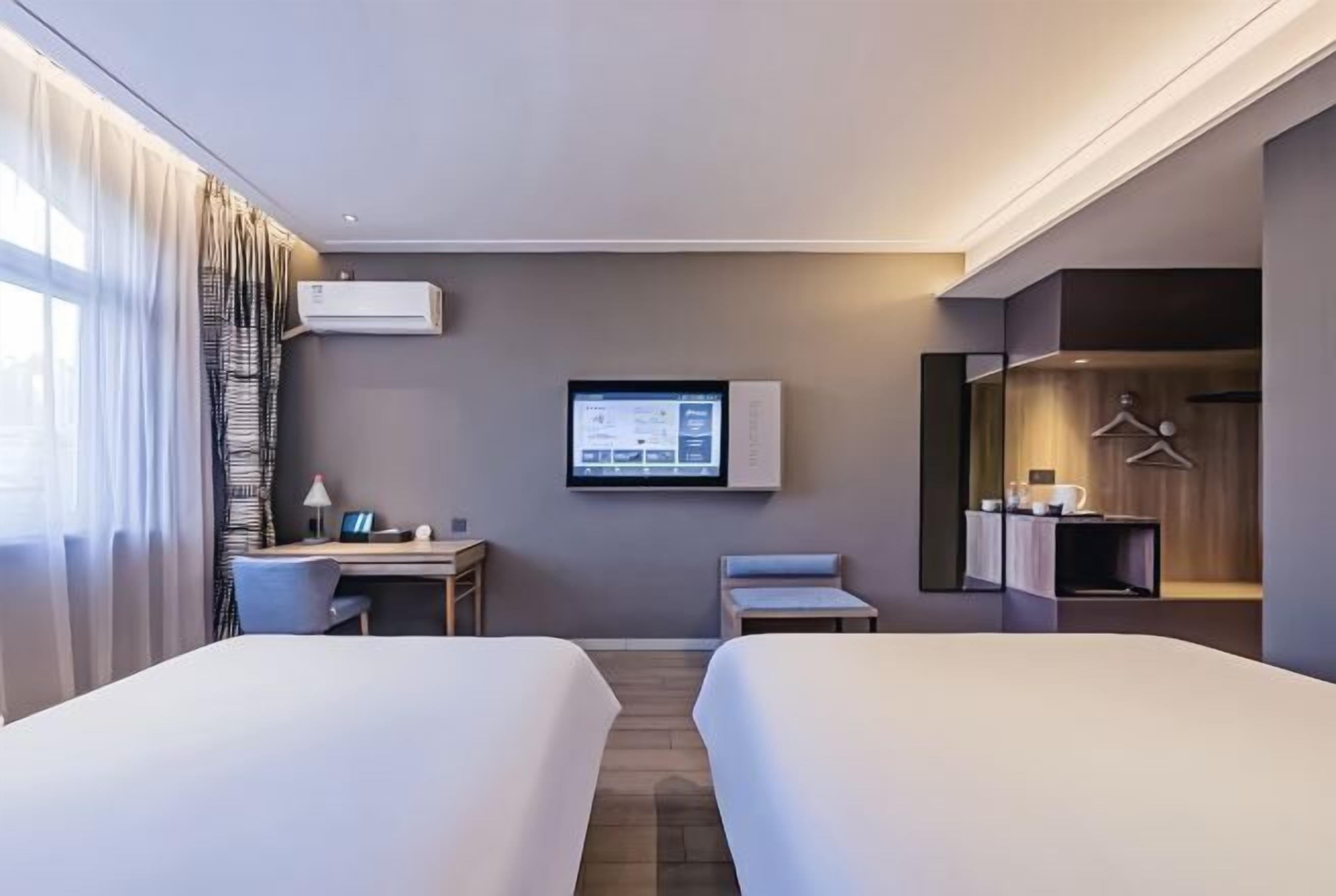A hotel room with two beds, a desk, a TV, and a wardrobe.