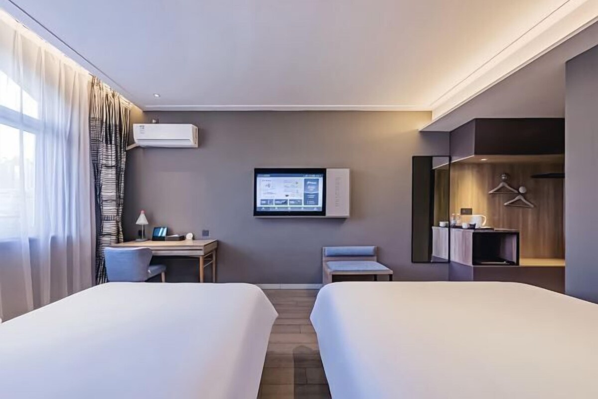 A hotel room with two beds, a desk, a TV, and a wardrobe.
