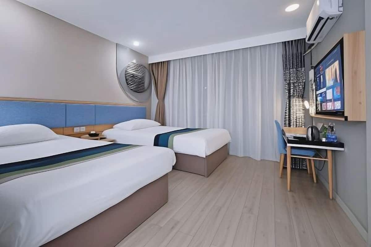 A hotel room with two beds, a desk, a chair, an air conditioning unit, and a television.