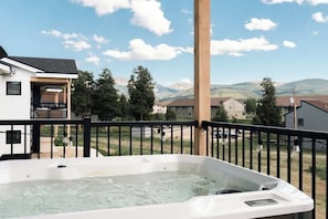 Un jacuzzi en un balcón con vista a la montaña, un poste de madera y una barandilla negra.