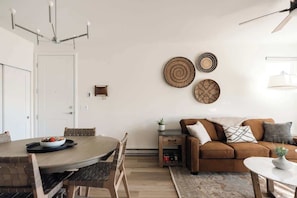 A modern living room with a dining table, brown sofa, and decorative wall art.