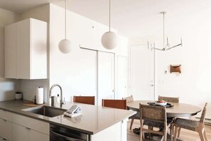 A modern kitchen with a central island, a dining area with a round table and chairs, and pendant lighting.