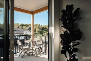 A balcony with a table and chairs, a view of a forested area, and a plant on the wall.