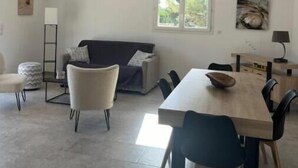 Ein modernes Wohnzimmer mit einer Couch, einem Esstisch und Stühlen. Ein Fenster bietet Blick auf Grünflächen.