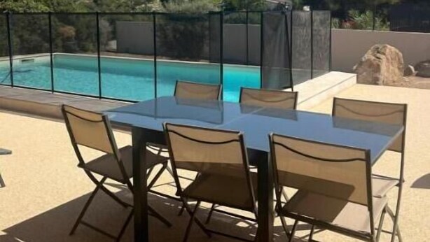 Ein Poolbereich mit Tisch und Stühlen, Blick auf Berge und wolkenlosen Himmel.