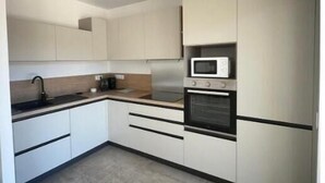 Eine moderne Küche mit weißen Schränken, einer schwarzen Arbeitsplatte, einem eingebauten Backofen und einer Mikrowelle.