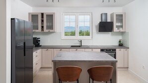 A modern kitchen with a central island, two bar stools, a built-in oven, and a large window with a view. - Luxury Villa Morus with pool 50m2, gym, family, bbq (Murvica)