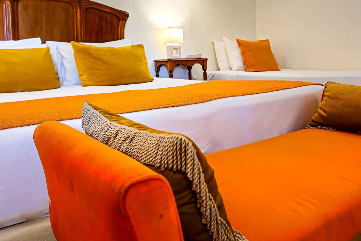 A hotel room with two beds, a wooden headboard, a chandelier, and a nightstand with a lamp.