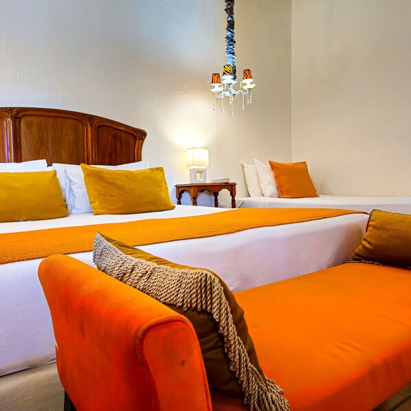 A hotel room with two beds, a wooden headboard, a chandelier, and a nightstand with a lamp.