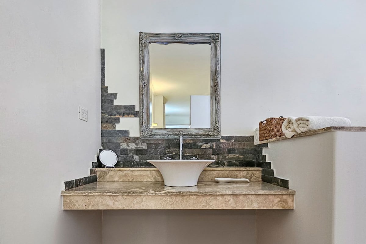 Une salle de bain avec un comptoir en pierre, un lavabo blanc, un miroir et un porte-serviettes.