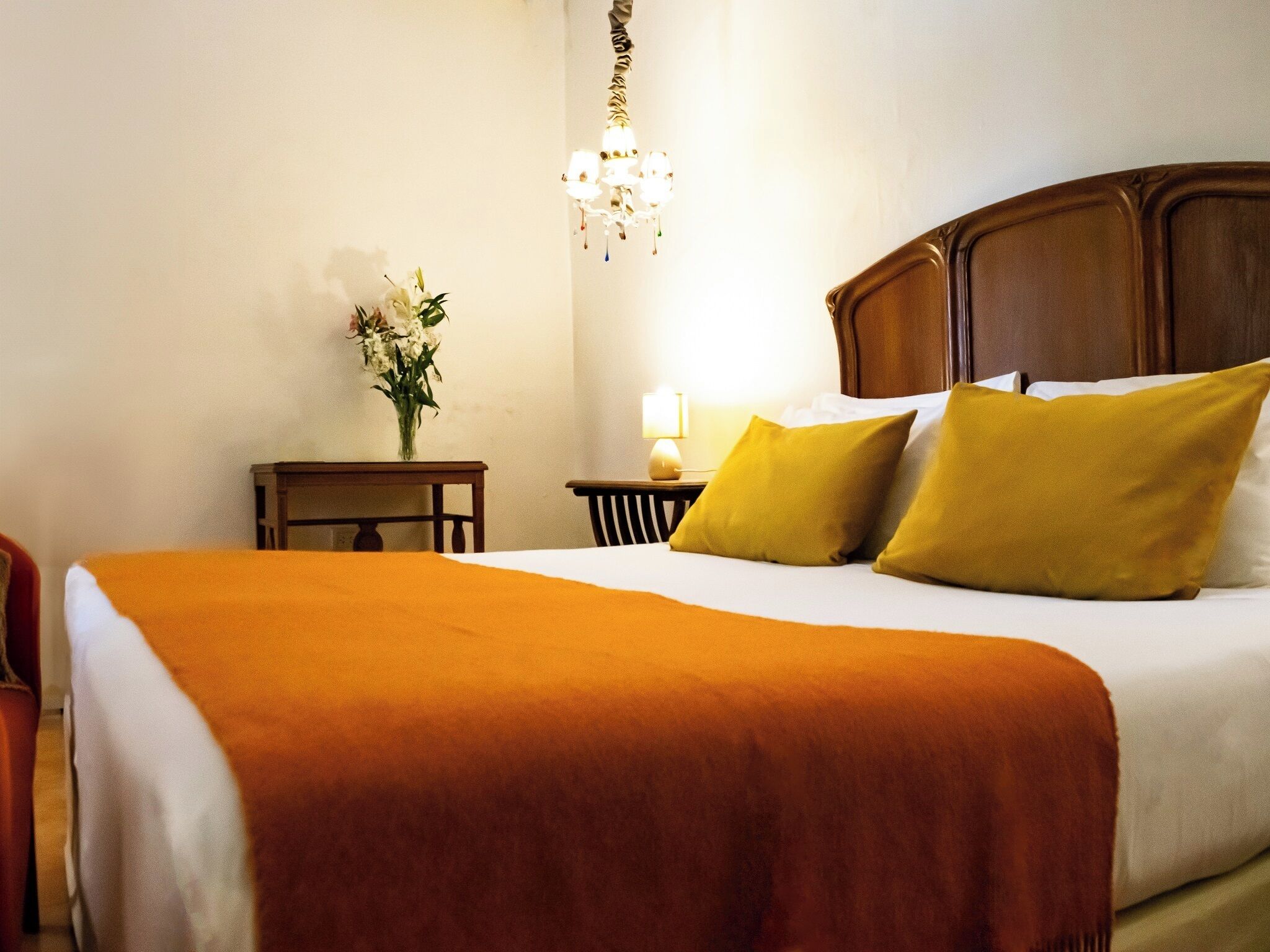 Una camera d'hotel con un letto grande, un comodino, una lampada e un vaso con fiori.