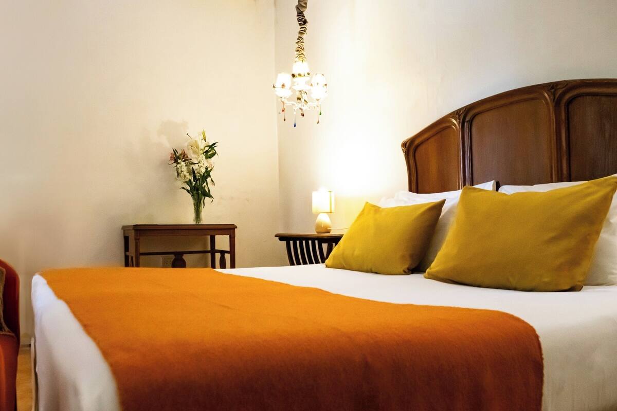 A hotel room with a large bed, a nightstand, a lamp, and a vase with flowers.