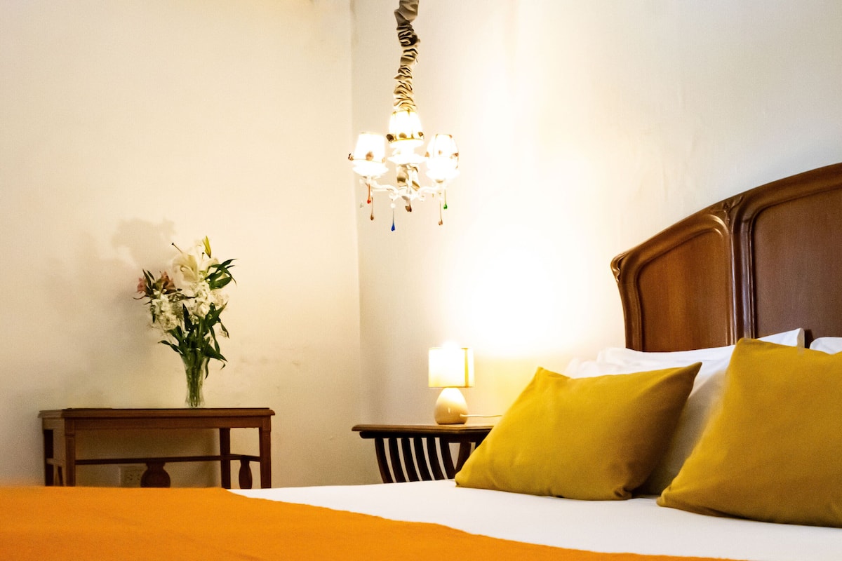 A hotel room with a bed, a nightstand, a lamp, and a chandelier.