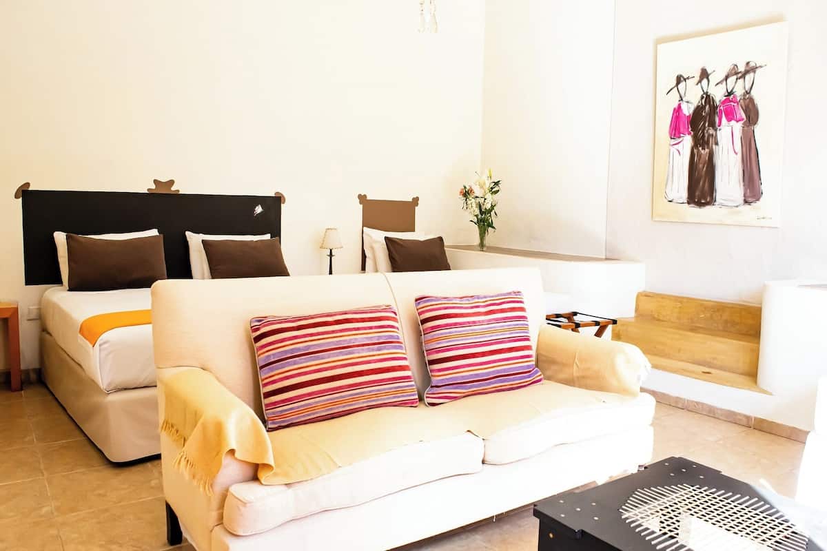 A hotel room with a bed, a sofa, a small table, and a painting on the wall.