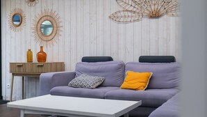 Una sala moderna con un sofá lavanda claro, una mesa de centro blanca y una mesita de noche de madera con dos botellas.