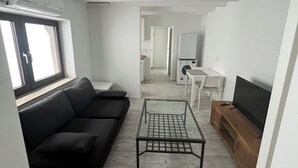 A compact living space with a sofa, a coffee table, a TV, and a washing machine in the background. - Krefeld Ruhiges Apartment in der 2. Etage. Mit Klimaanlage (Krefeld)