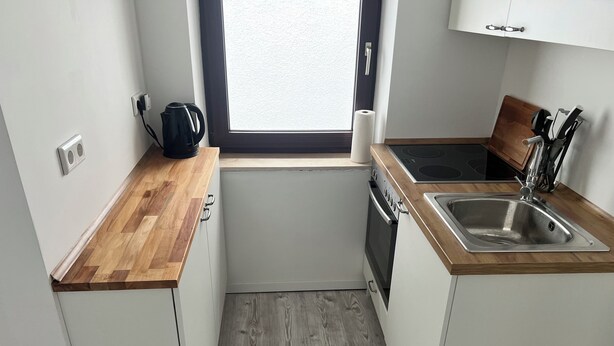 A compact kitchen with a wooden countertop, a built-in oven, a sink, and a window with a view. - Krefeld Ruhiges Apartment in der 2. Etage. Mit Klimaanlage (Krefeld)