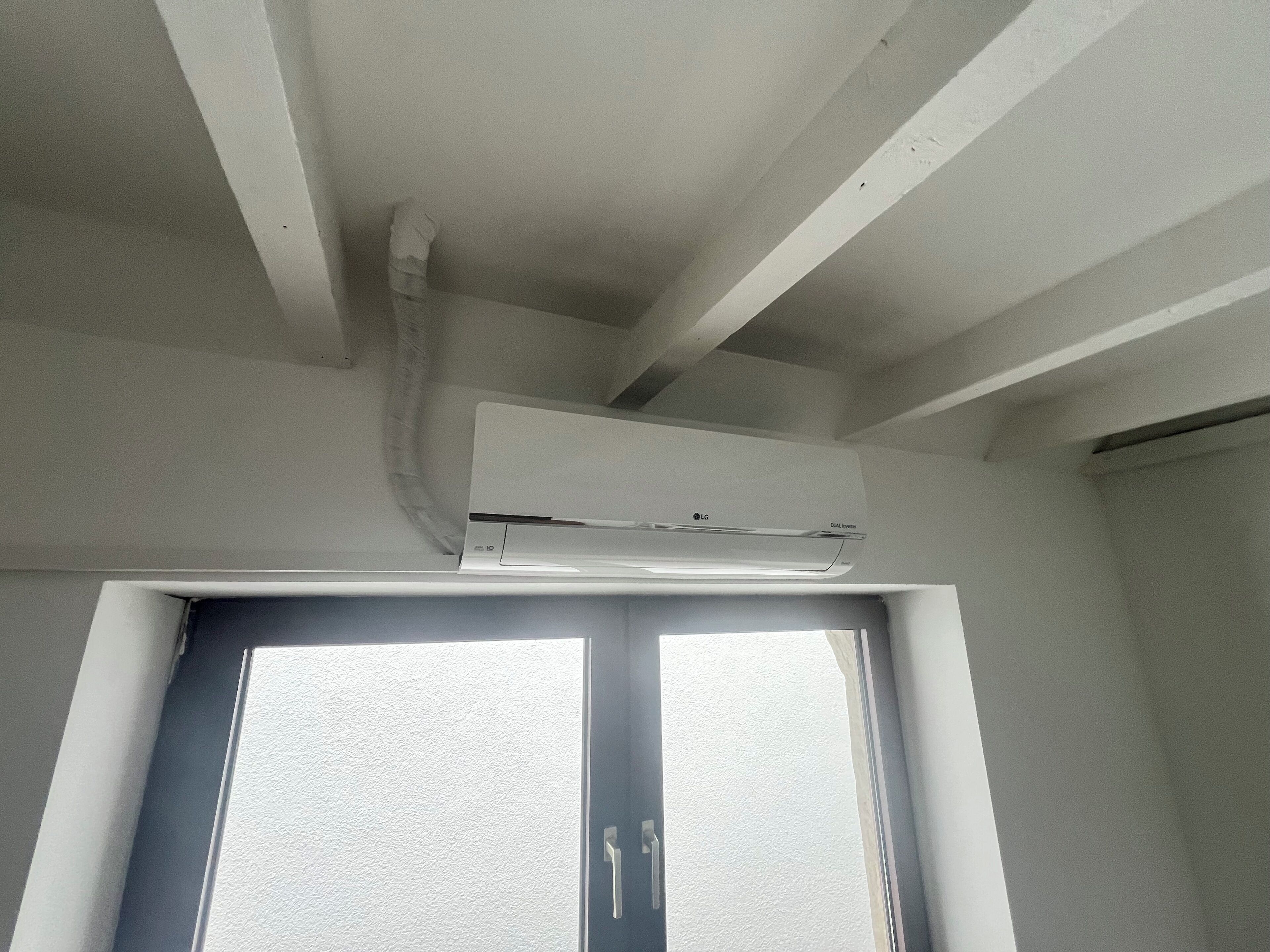 Et rum med en hvid airconditionenhed monteret på loftet over en dør med en struktureret, hvid dørkarm.