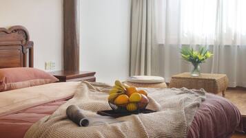 Ein ordentlich bezogenes Bett mit einer gestrickten Decke, ein Nachttisch mit Obstschale und eine Lampe.
