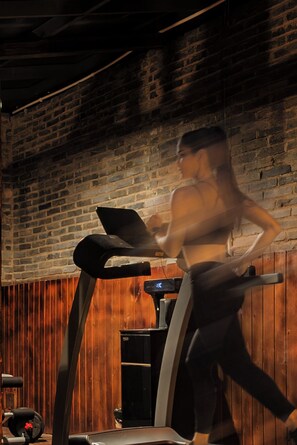 A person using a treadmill in a room with a brick wall and wooden paneling. - Full moon Inn Lijiang (Lijiang)