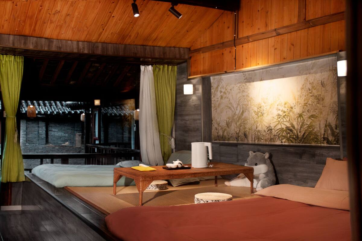 Een kamer met een bed, een tafel met waterkoker, een pluchen knuffel en een muur met een plantenmuur.