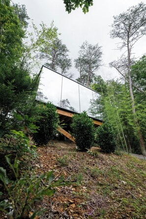 A modern building with a sloped roof, surrounded by dense foliage and trees.