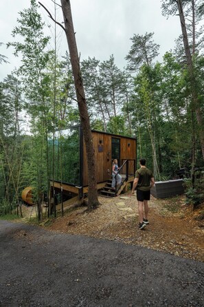 Una cabaña de madera con una escalera que lleva a una terraza, rodeada de un bosque.