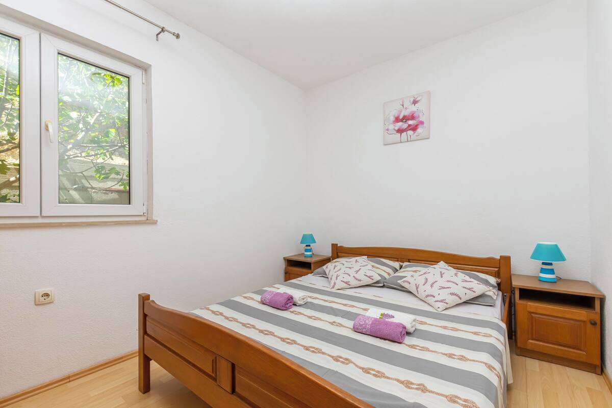 A bedroom with a wooden bed, two bedside tables, a window, and a wall-mounted picture.
