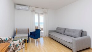En moderne stue med en grå sofa, en blå lænestol, et glasbord og et træ sofabord.