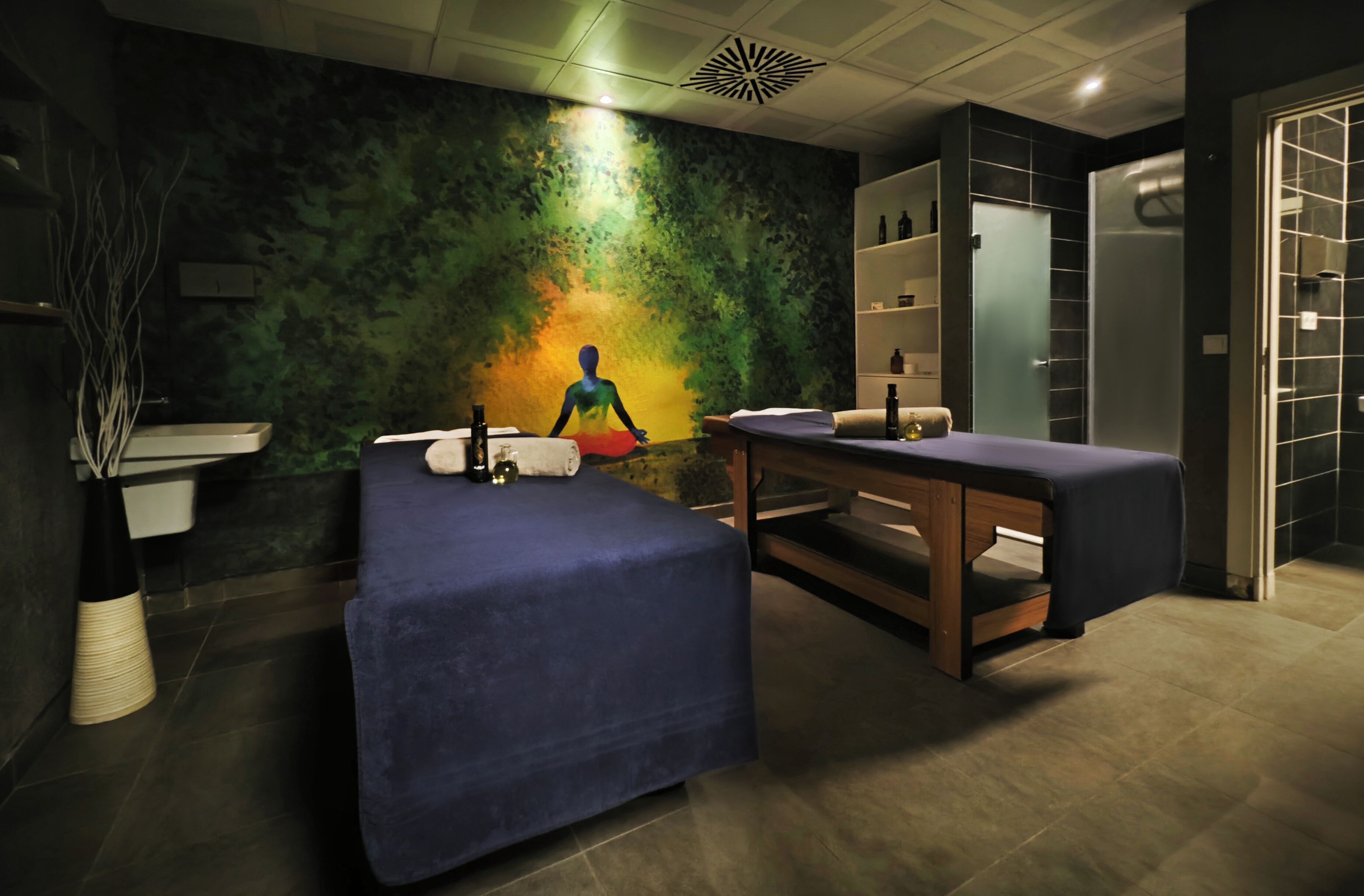 A modern spa room with a massage table, a small sink, and a shelf with bottles.