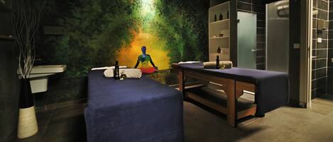 A modern spa room with a massage table, a small sink, and a shelf with bottles.