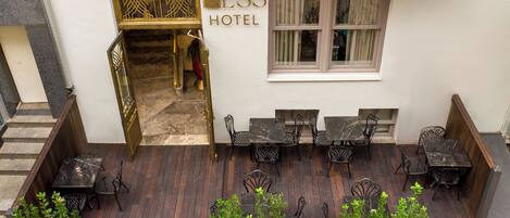 A hotel entrance with a sign reading "ESS HOTEL," a wooden deck with outdoor seating, and a staircase leading to the entrance.