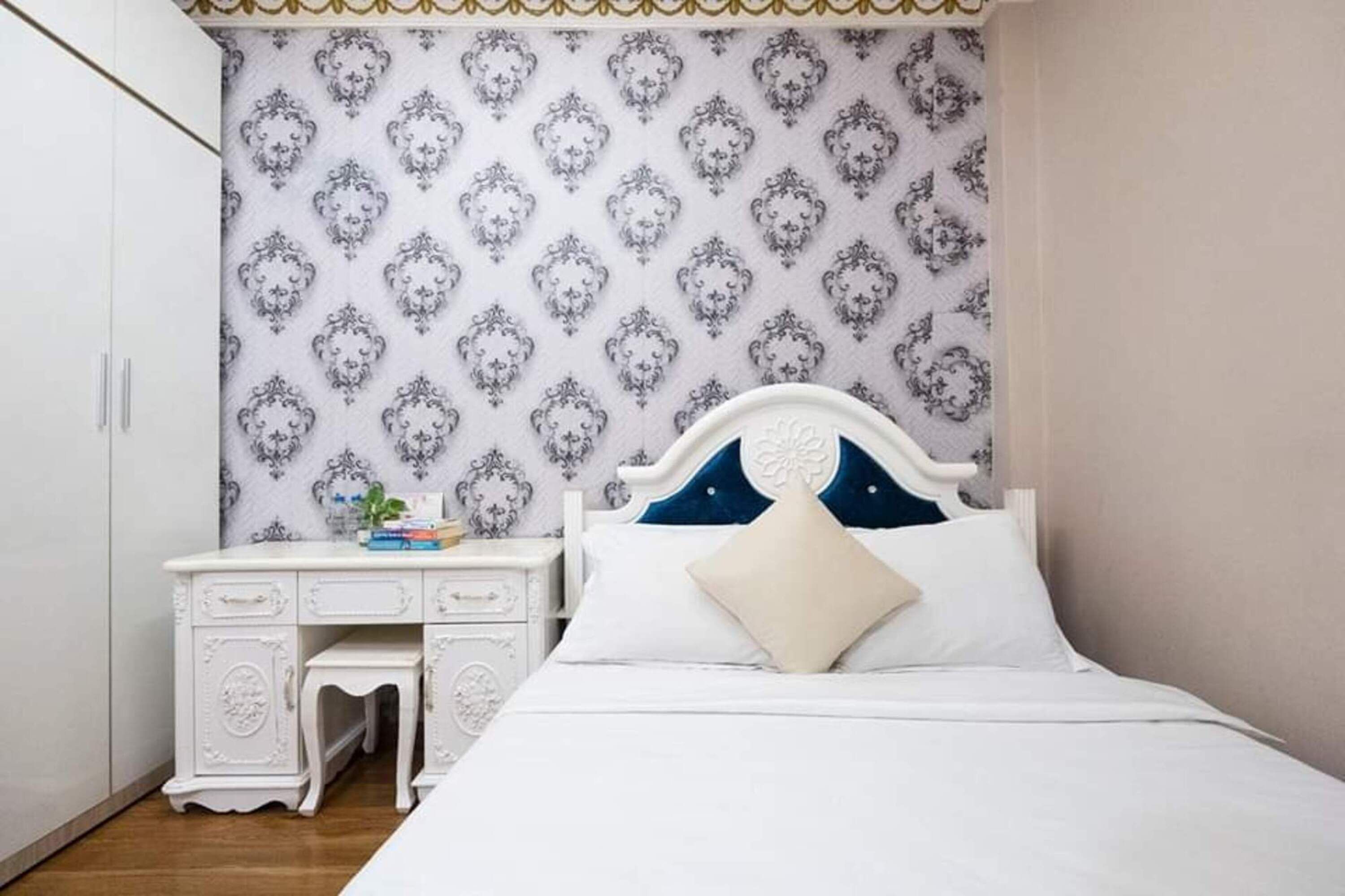 Un dormitorio con una cama, un aparador blanco y un papel tapiz estampado.