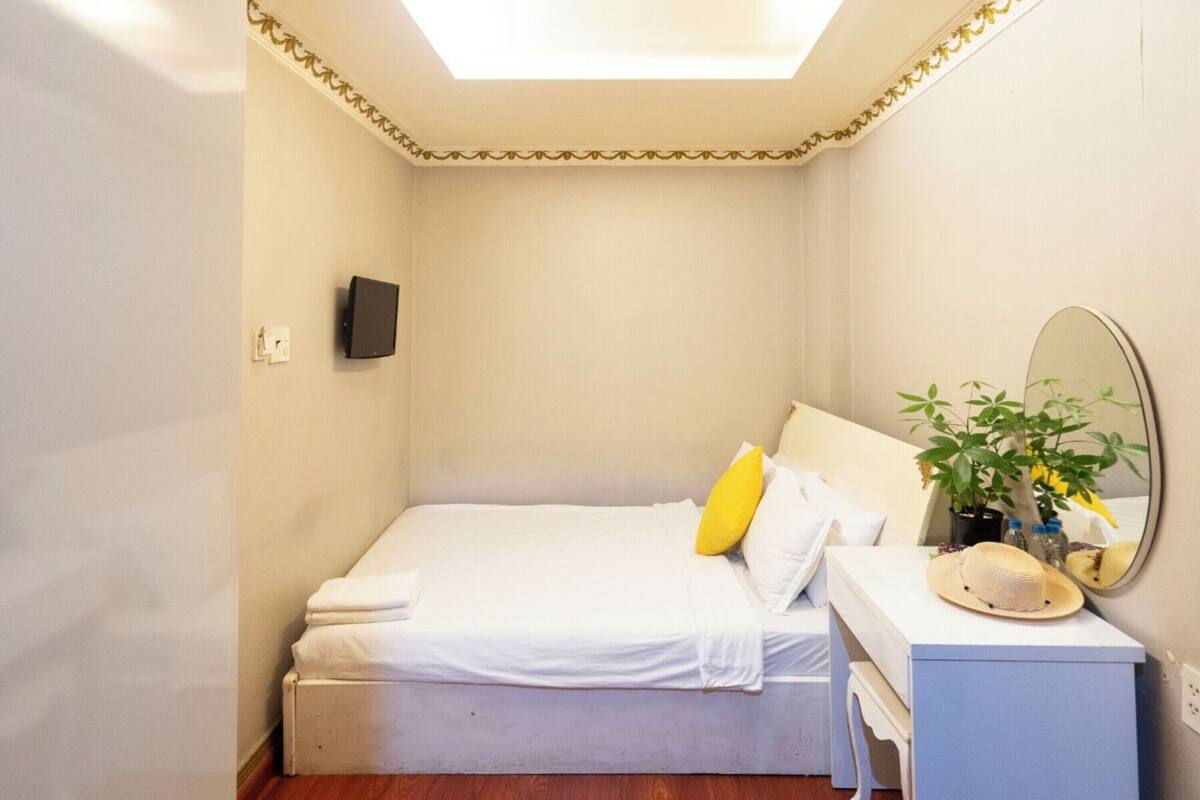 Un dormitorio pequeño y ordenado con cama, mesita de noche, espejo y una planta en maceta.
