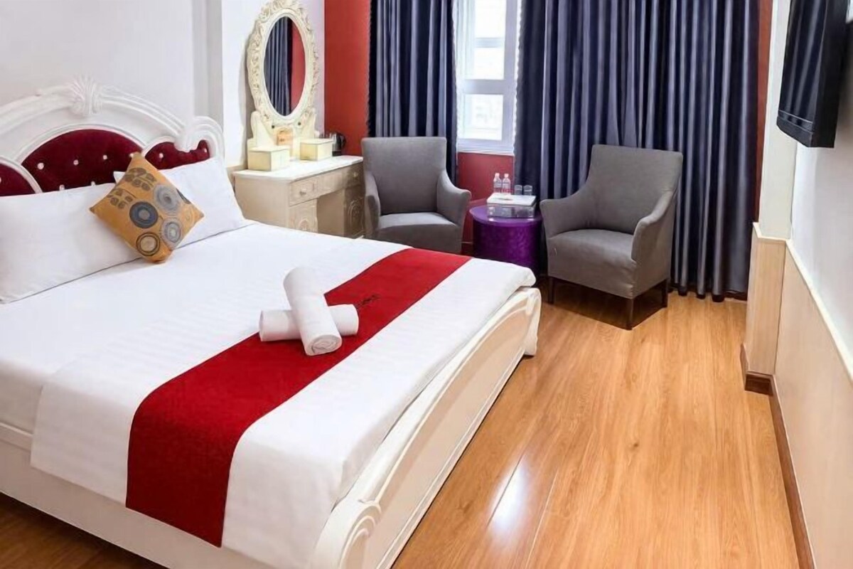 Une chambre d’hôtel comprenant un lit, deux fauteuils, une coiffeuse avec un miroir et un téléviseur.