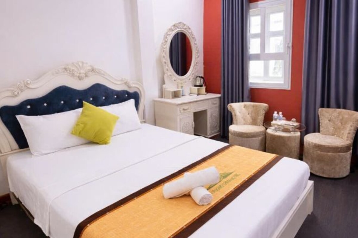 Una habitación de hotel con una cama, un tocador con espejo, dos sillones y una ventana con cortinas.