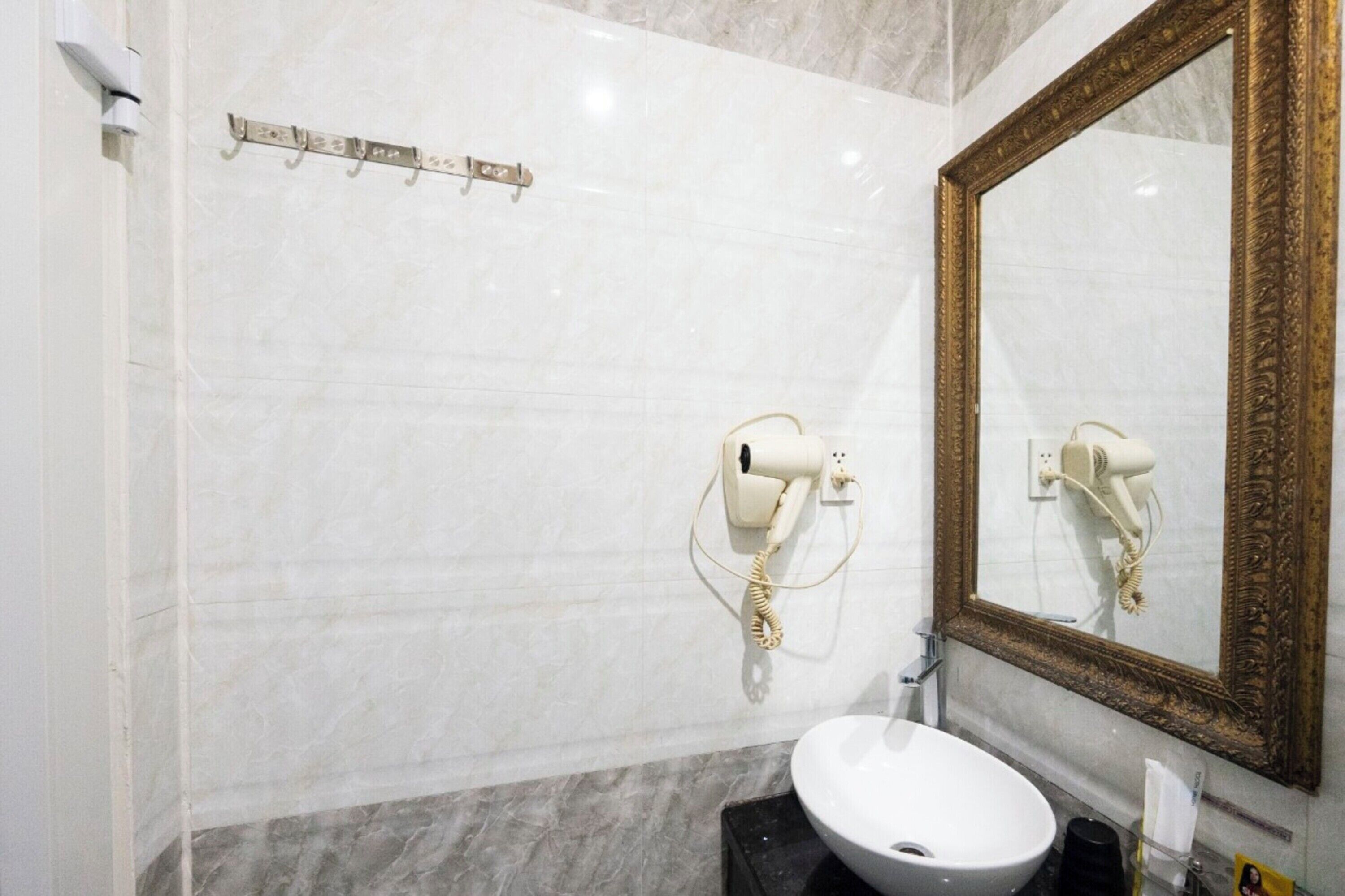 Un bagno con parete in marmo, uno specchio con cornice dorata, un lavandino bianco e un asciugacapelli montato a parete.