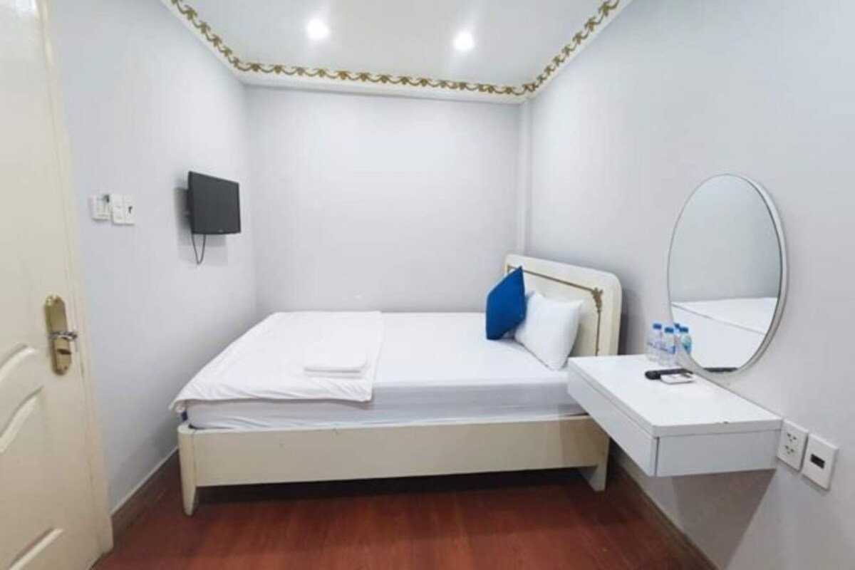Una habitación pequeña y limpia con cama, mesita de noche, espejo y televisor montado en la pared.