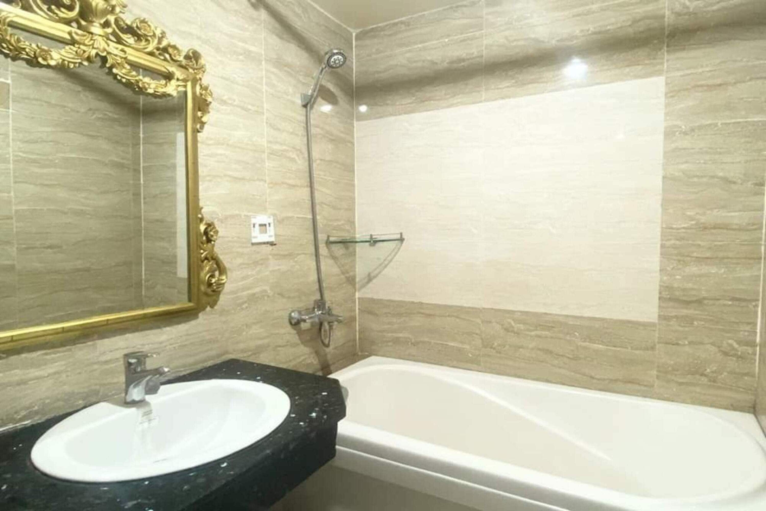 Un baño con una bañera blanca, un lavabo de mármol negro y un espejo con marco dorado.