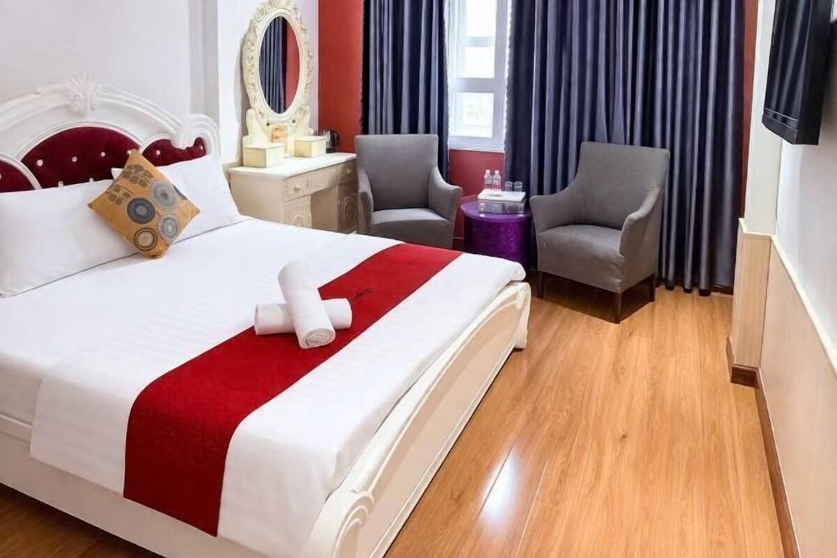Una habitación de hotel con una cama, dos sillones, un tocador con espejo y un televisor.