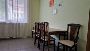 Ein Essbereich mit einem Holztisch und vier Stühlen. Ein Fenster mit leichtem Vorhang, und die Wand ist schlicht gestaltet, mit zwei kleinen Bildern.