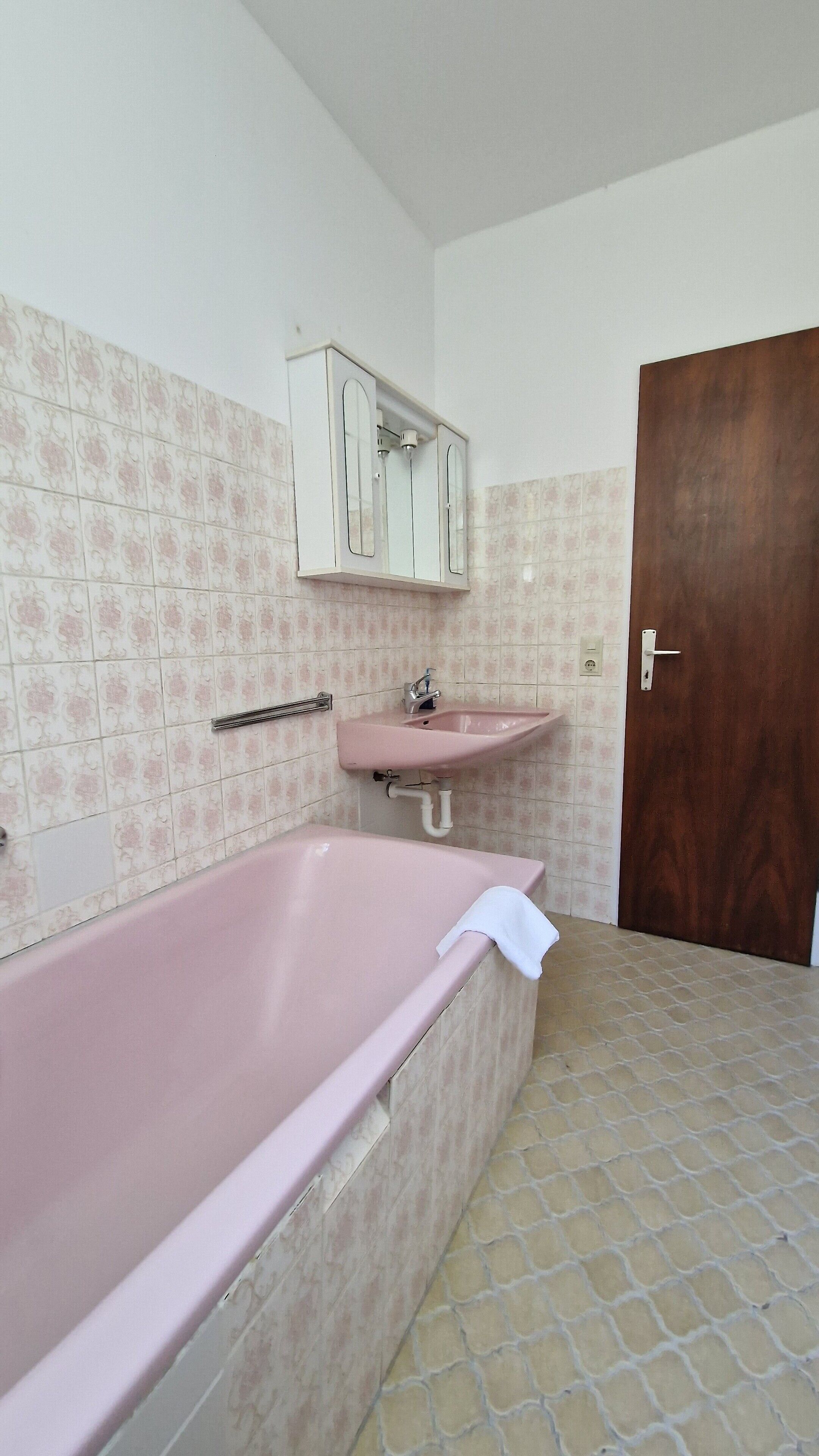 A bathroom with a pink bathtub, a sink, and a wooden door.