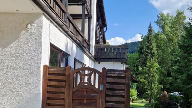 Ein hölzernes Tor mit einem Metallgriff, eine pflasterbelagte Fläche und ein Balkon mit Metallgeländer.