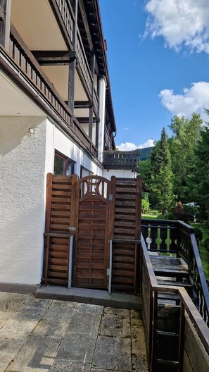 En træport med metalgreb, et brostensbelagt område og en balkon med metalgelænder.