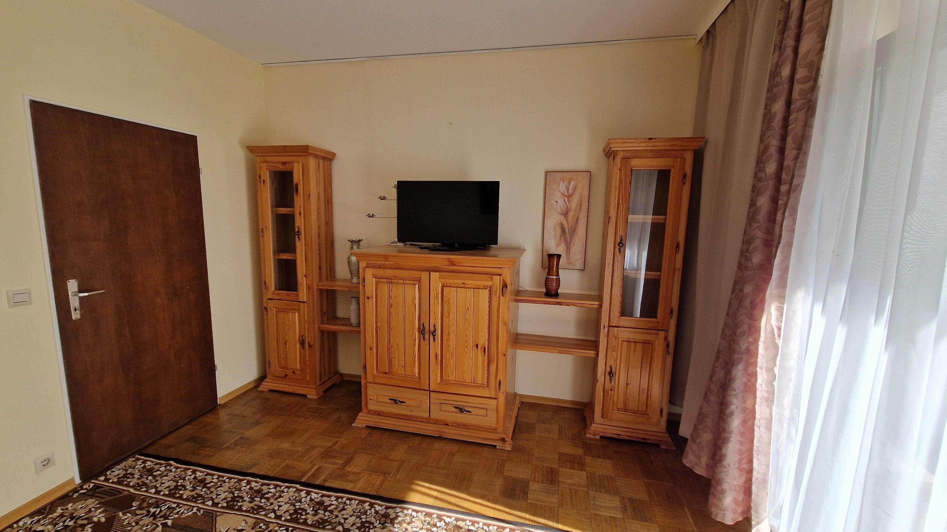 Een kamer met houten kasten, een televisie en een kamerkleed met een patroon.